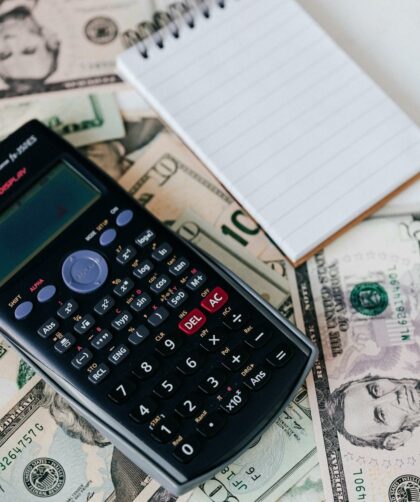 calculator and notepad placed on usa dollars stack